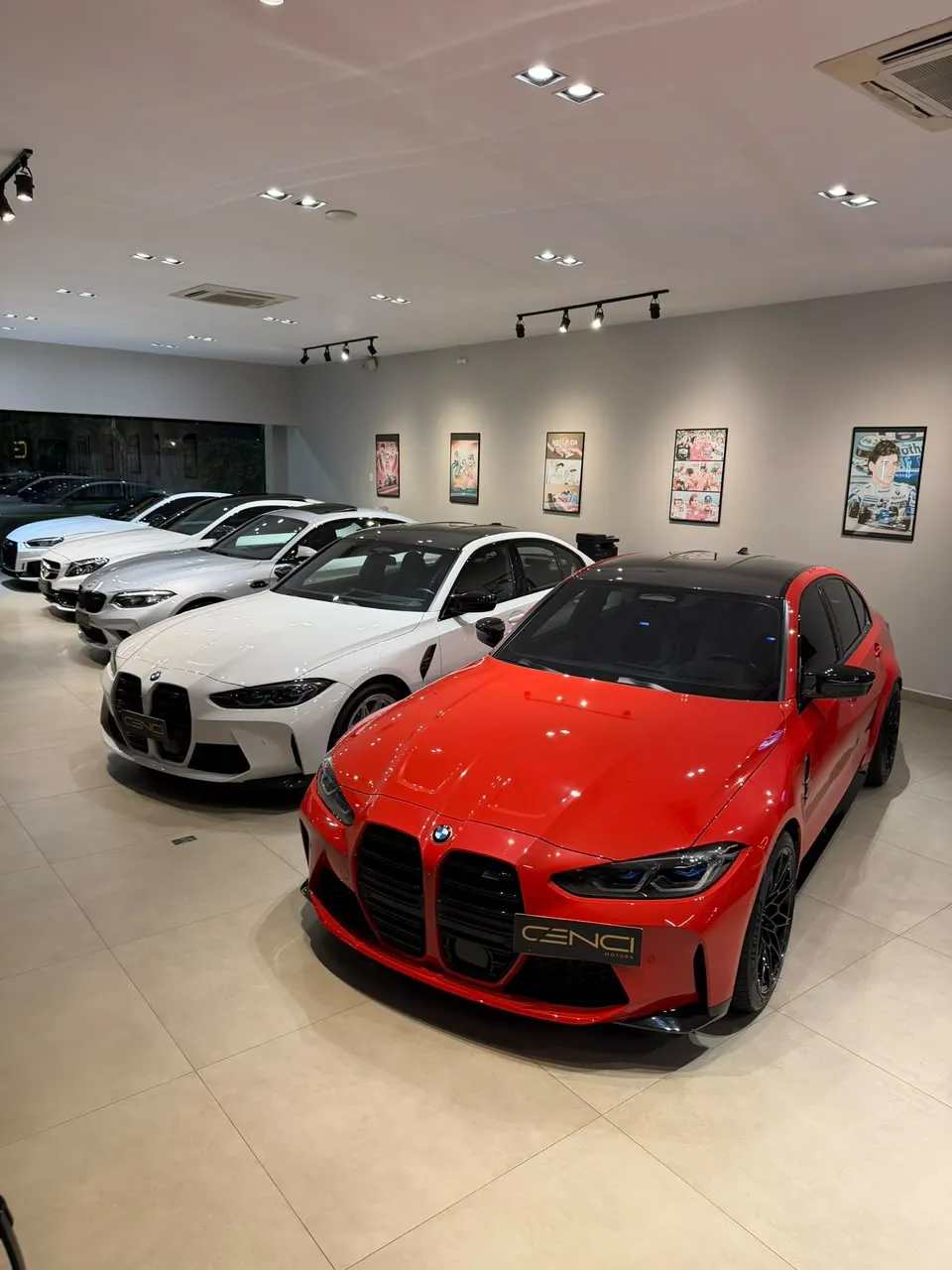 BMW M3 vermelha em primeiro plano e fileira de carros brancos no salão da Cenci Motors