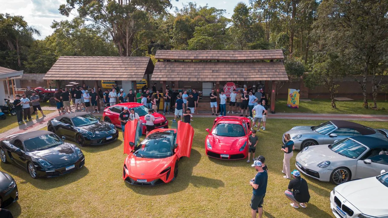 Carros esportivos expostos no gramado, com uma McLaren laranja de portas abertas e o público em volta